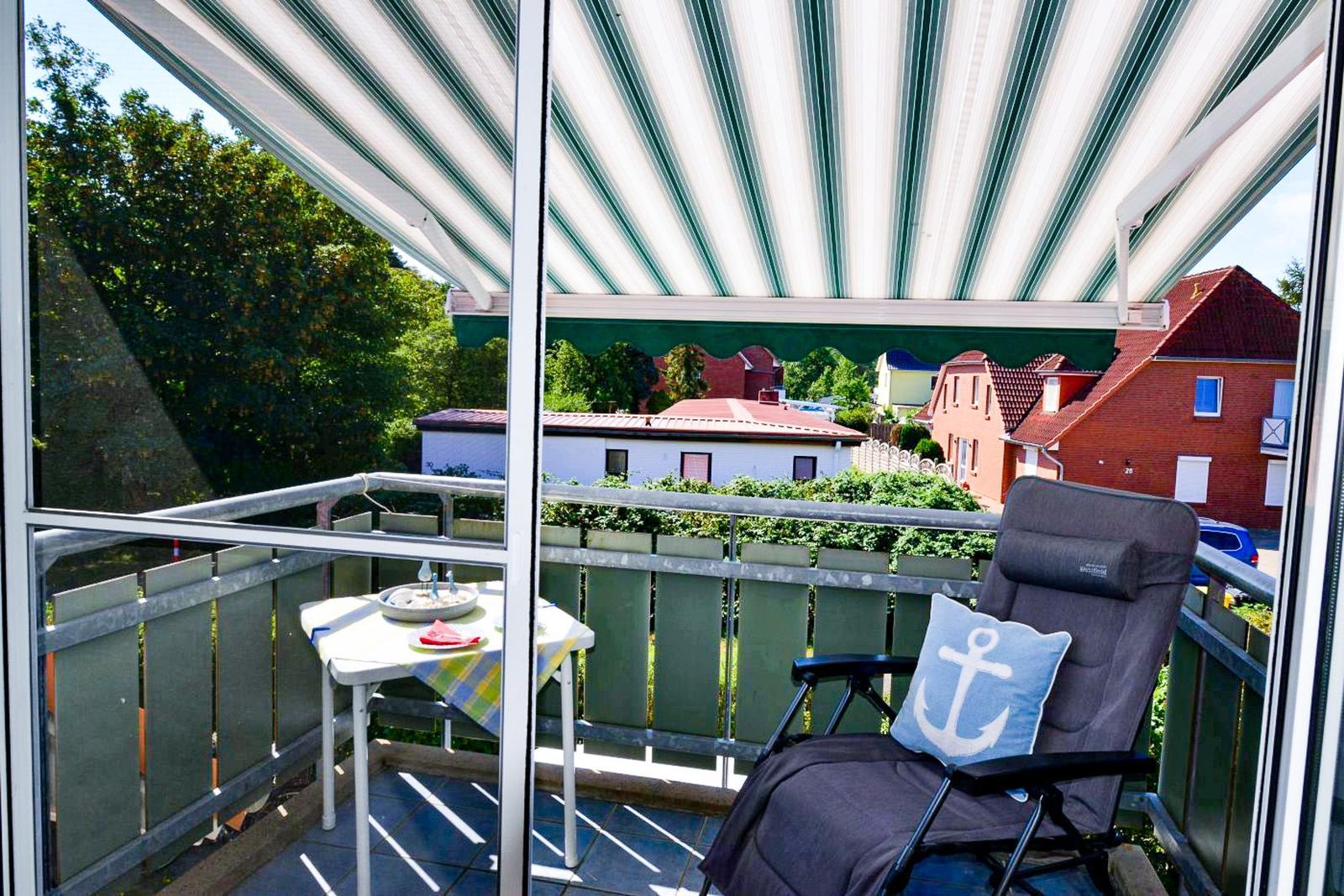 Terrasse mit Sonnenschutz, Stuhl und Tisch. Blick auf Wohnhäuser und Bäume.