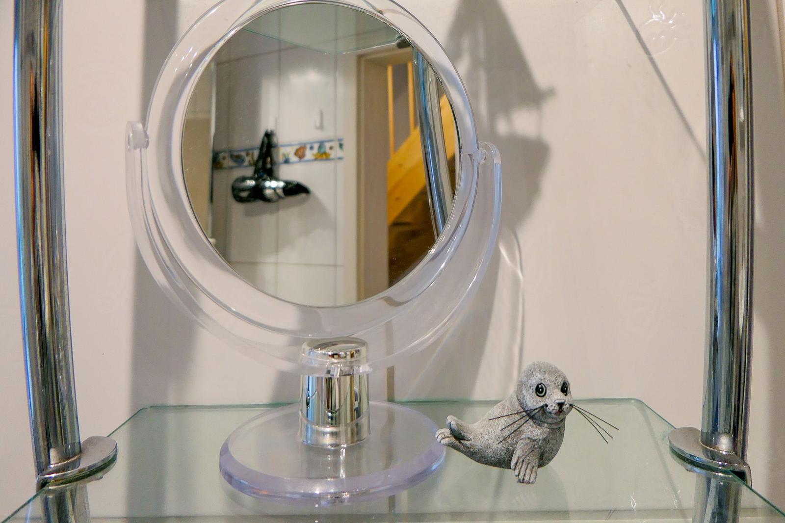 Ein runder Spiegel auf Glas steht neben einer Seehundfigur.