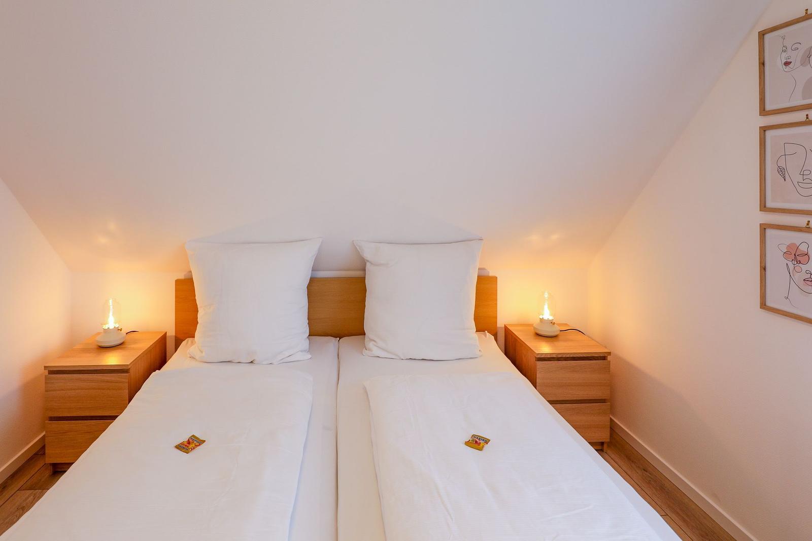 Doppelbett mit zwei Nachttischen und Lampen unter schrägen Dachschrägen.