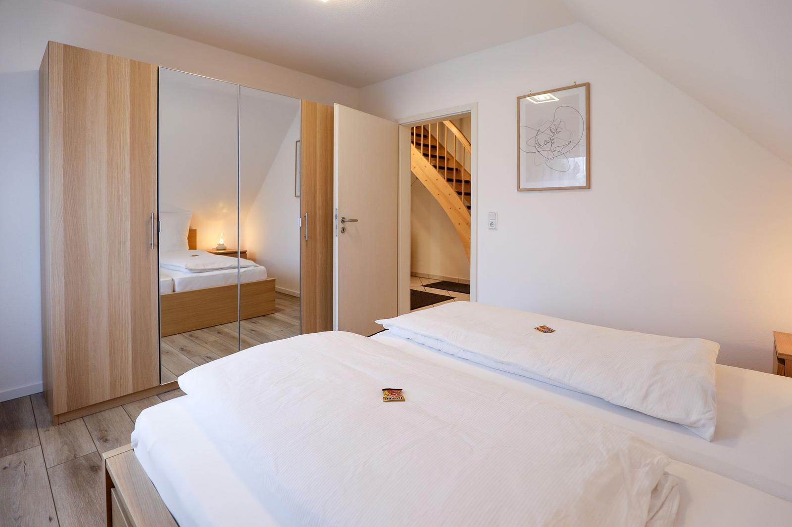 Schlafzimmer mit Doppelbett, Spiegelschrank und Blick auf Treppe.
