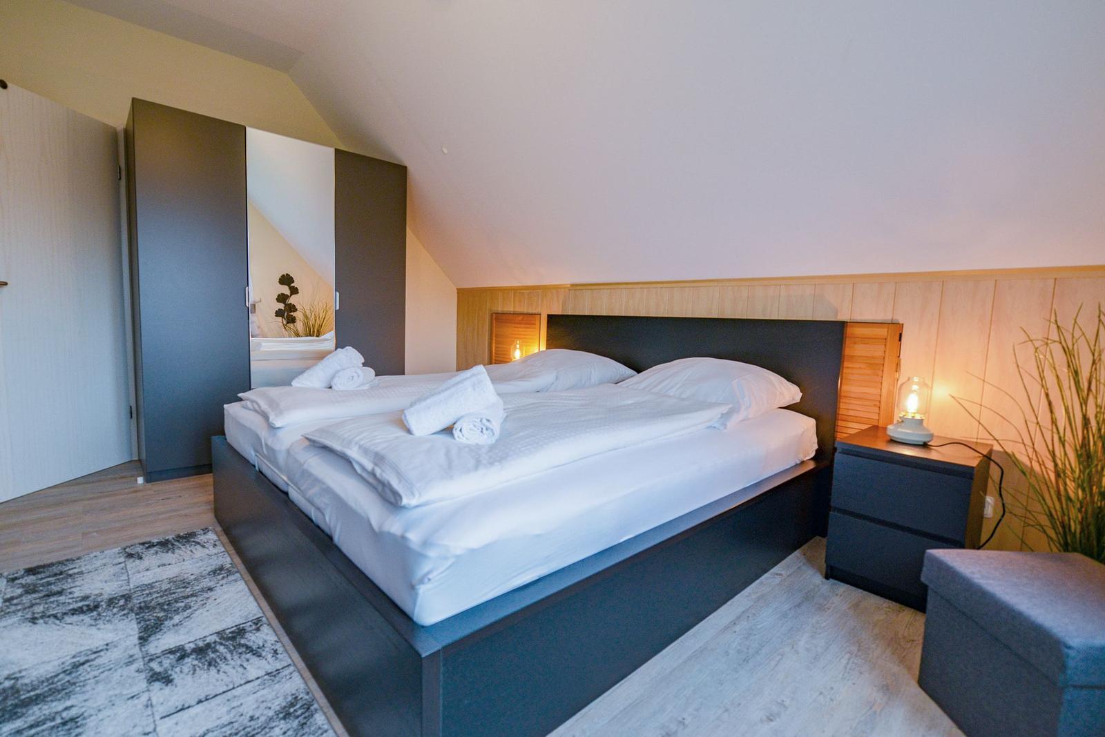 Schlafzimmer mit Doppelbett, Nachttisch und Schrank unter schräger Decke.