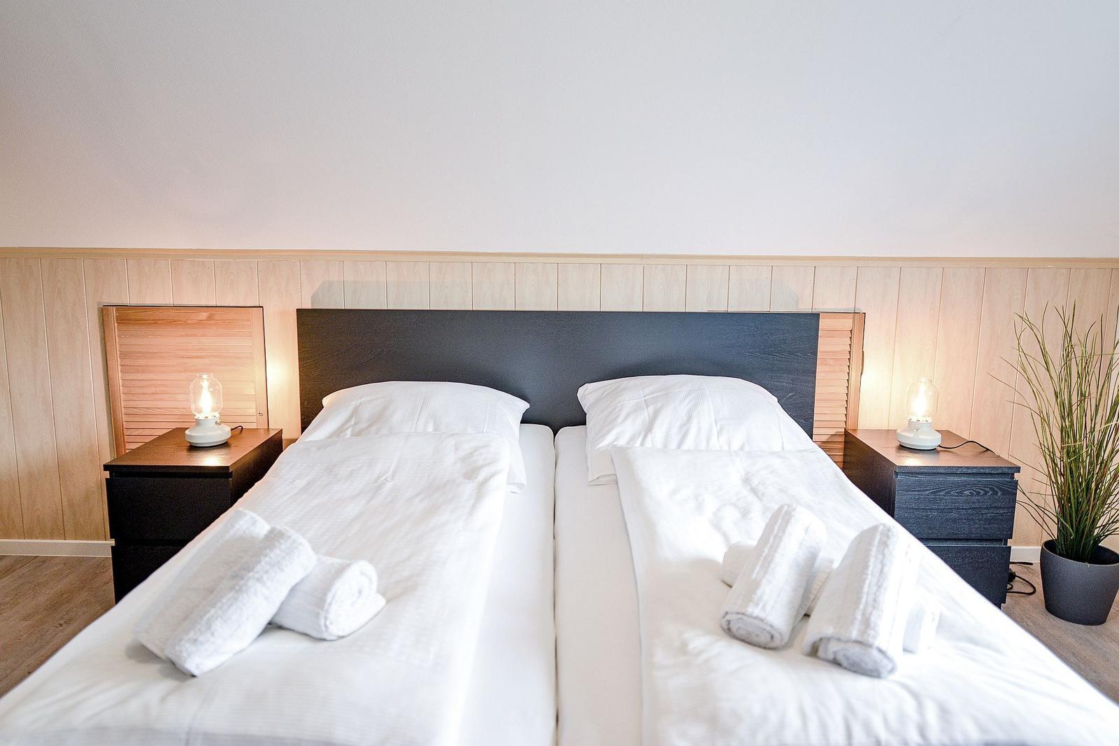 Zwei Betten mit weißen Laken und Handtüchern, Nachttische mit Lampen und Pflanze.