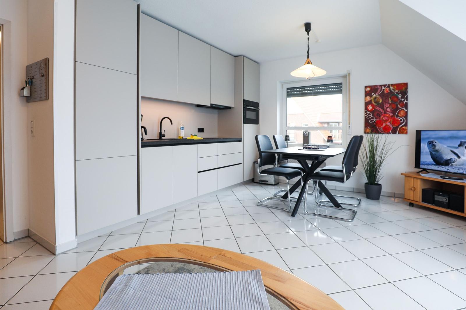 Moderne Küche mit Essbereich und Wohnzimmer mit Fernseher und Wandbild.
