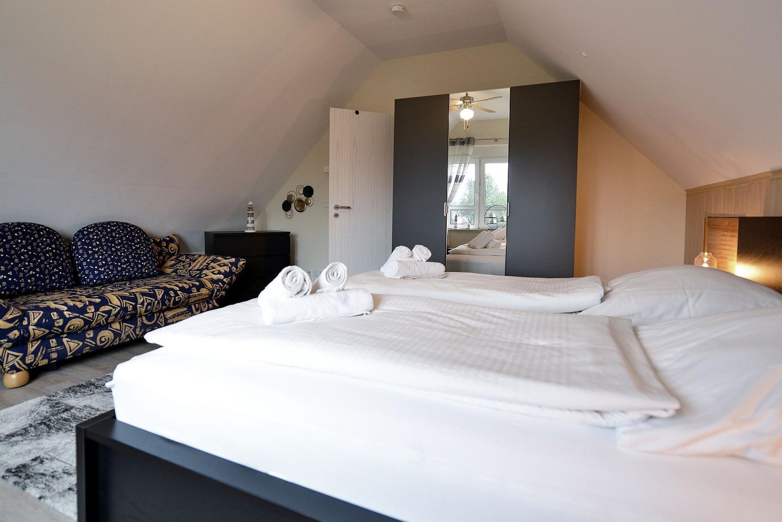 Schlafzimmer mit Doppelbett, Sofa und Spiegelschrank. Dachgeschoss mit geneigtem Dach.