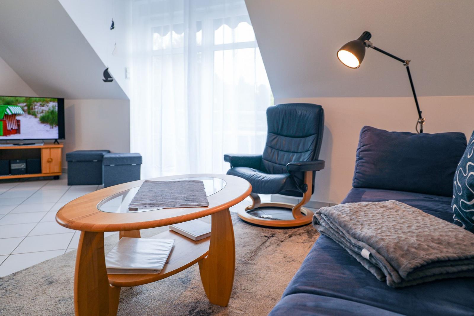 Wohnzimmer mit Sofa, Sessel, Tisch und TV unter Dachschrägen.