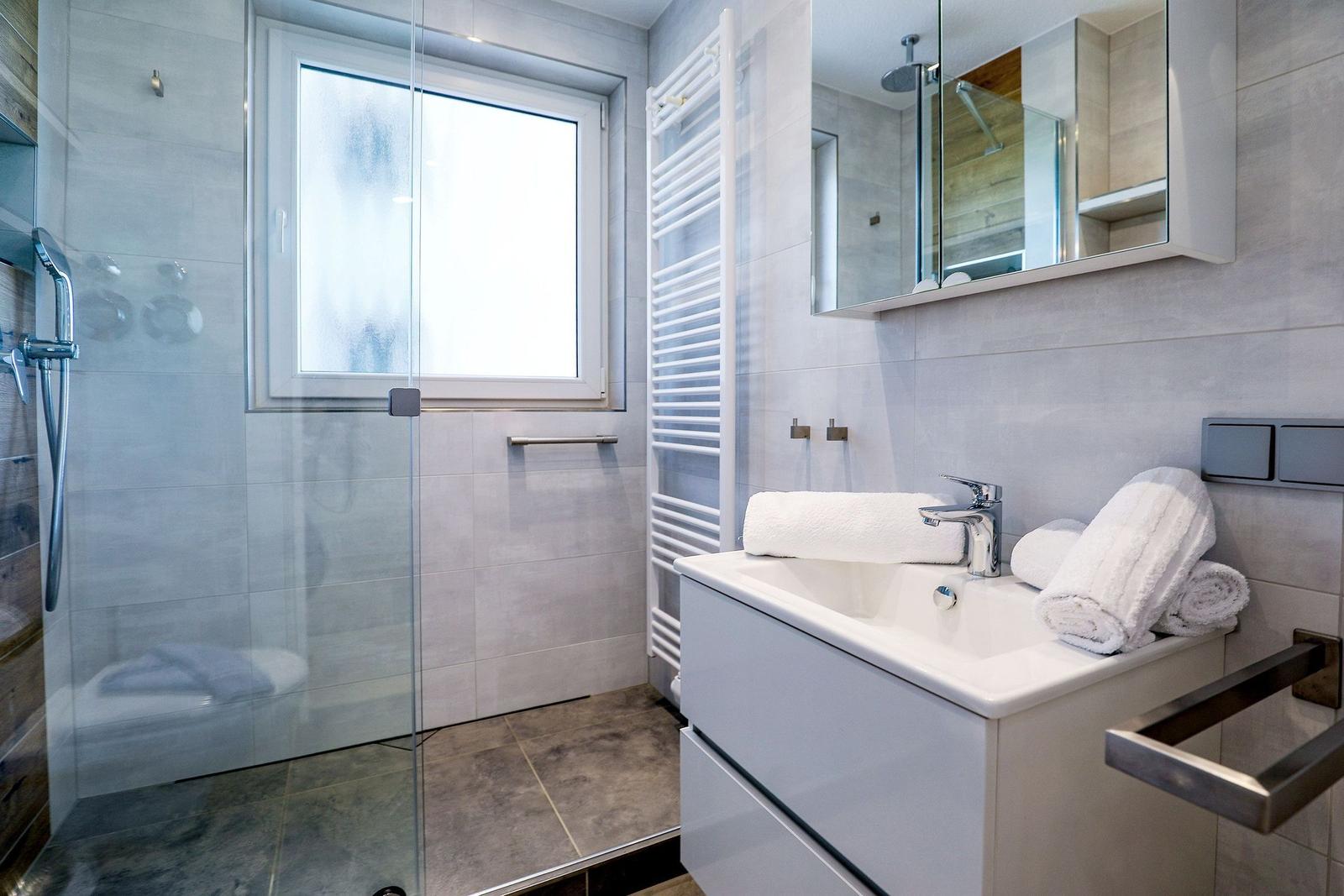 Badezimmer mit Dusche, Waschbecken und Spiegel.