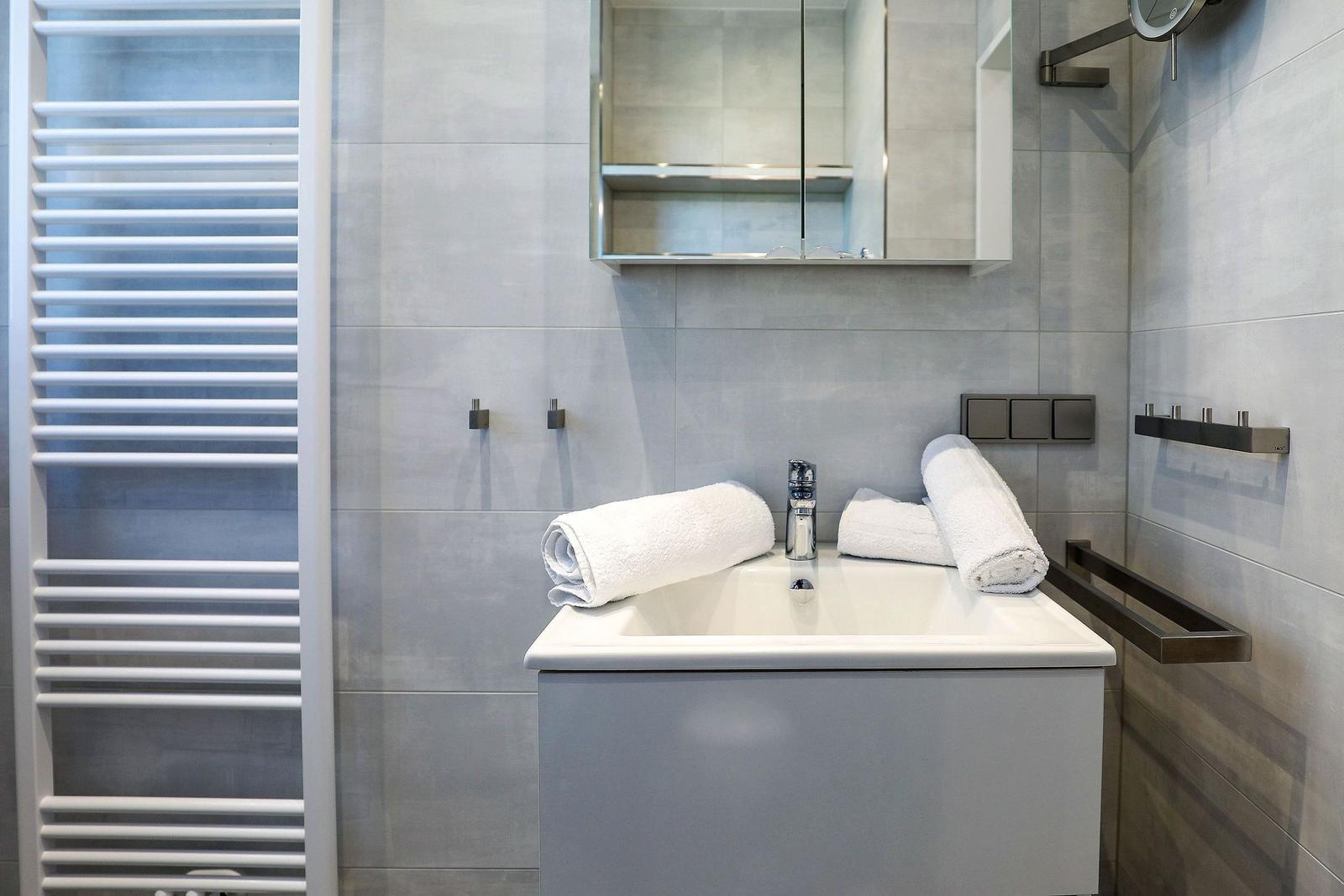 Badezimmer mit Waschbecken, Spiegel, Handtuchhalter und Heizkörper.