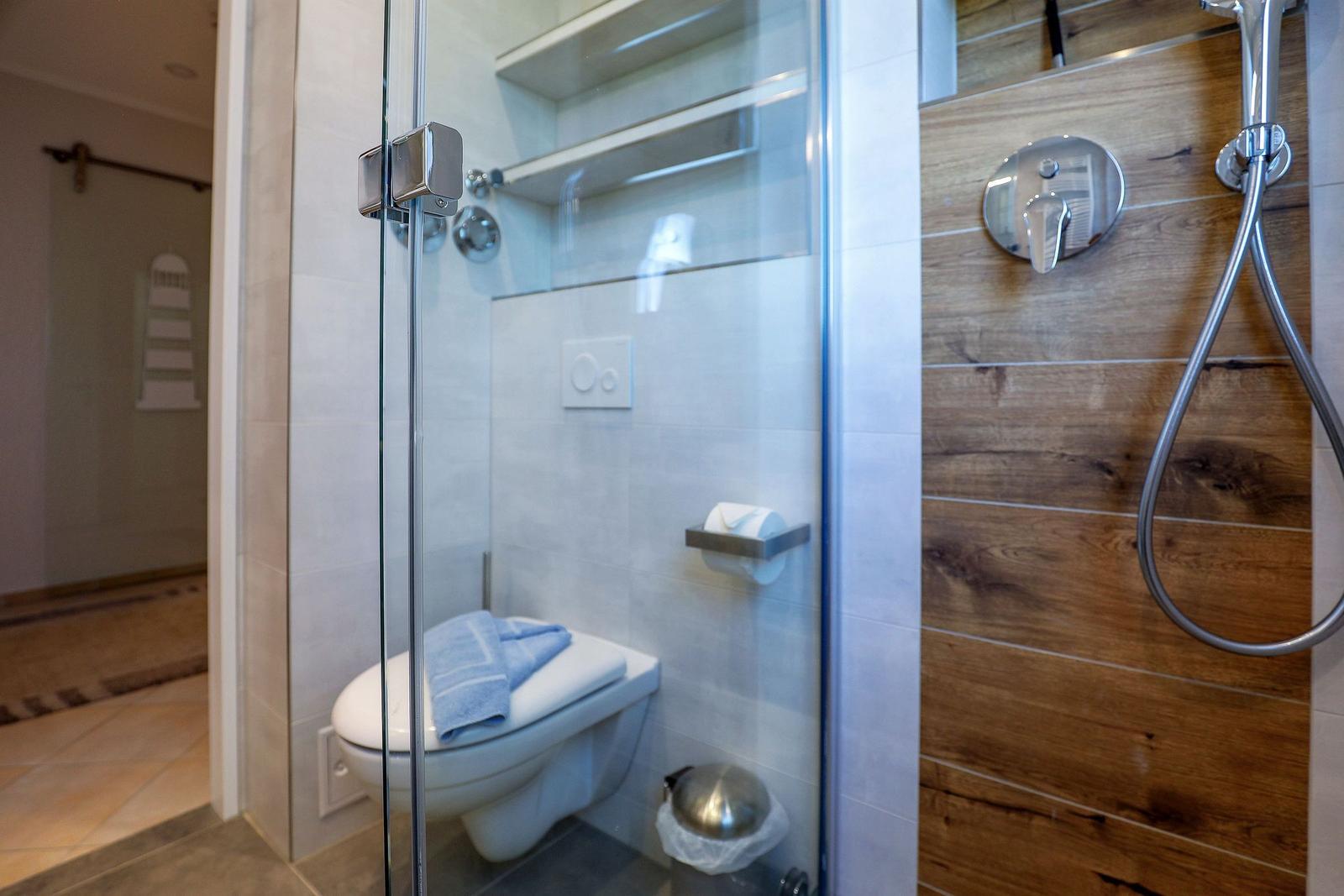 Dusche mit Holzfliesen und Toilette hinter Glaswand