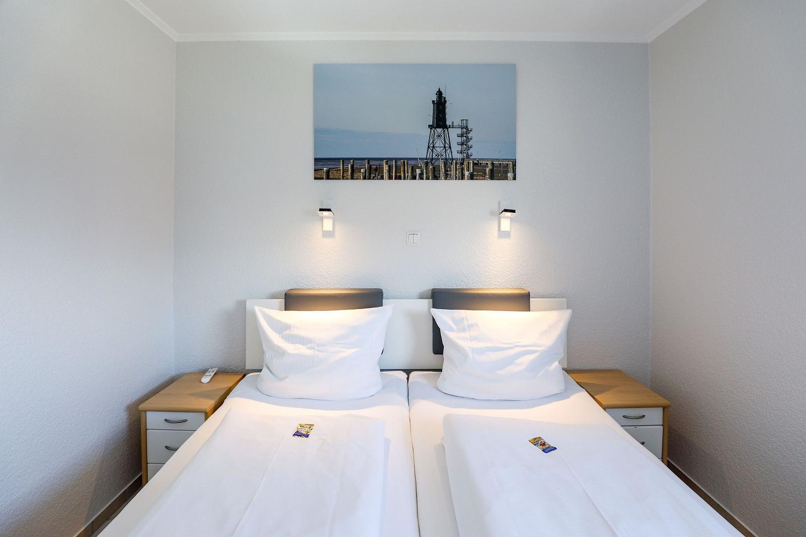 Zwei Einzelbetten mit weißen Bettwäsche und Nachttischen. Wandbild zeigt Leuchtturm.