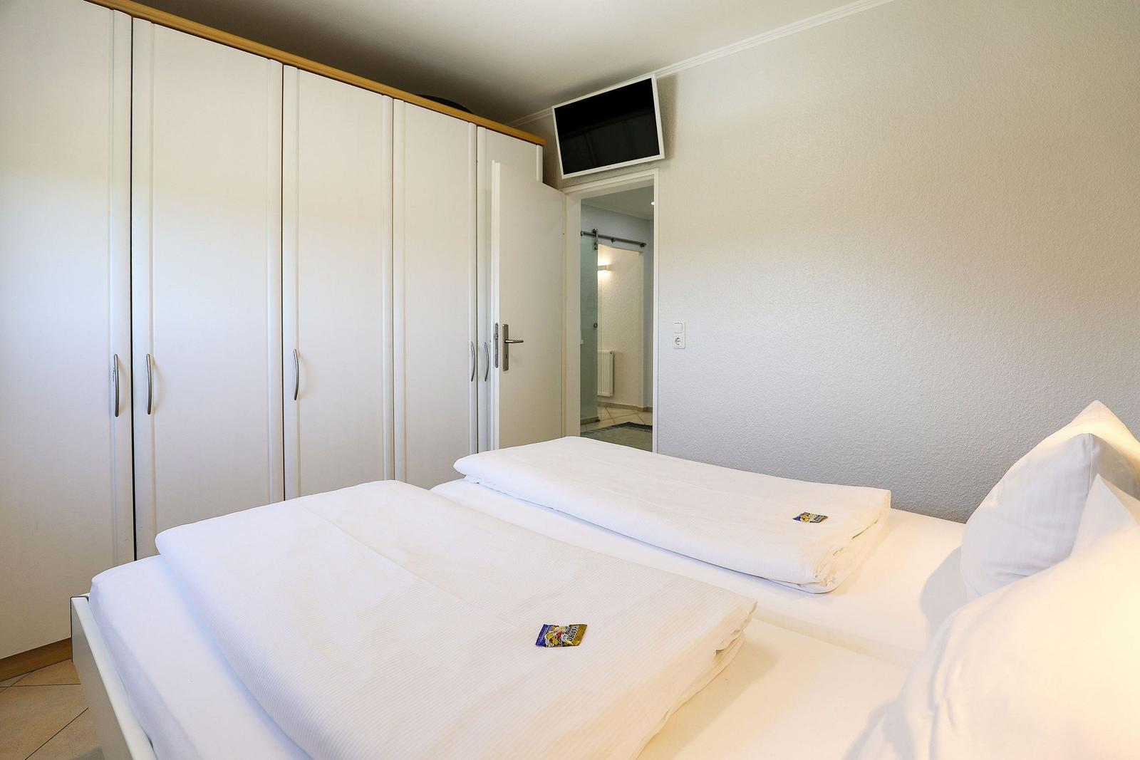 Zimmer mit zwei Betten, Kleiderschrank und TV. Blick in die Badezimmer.