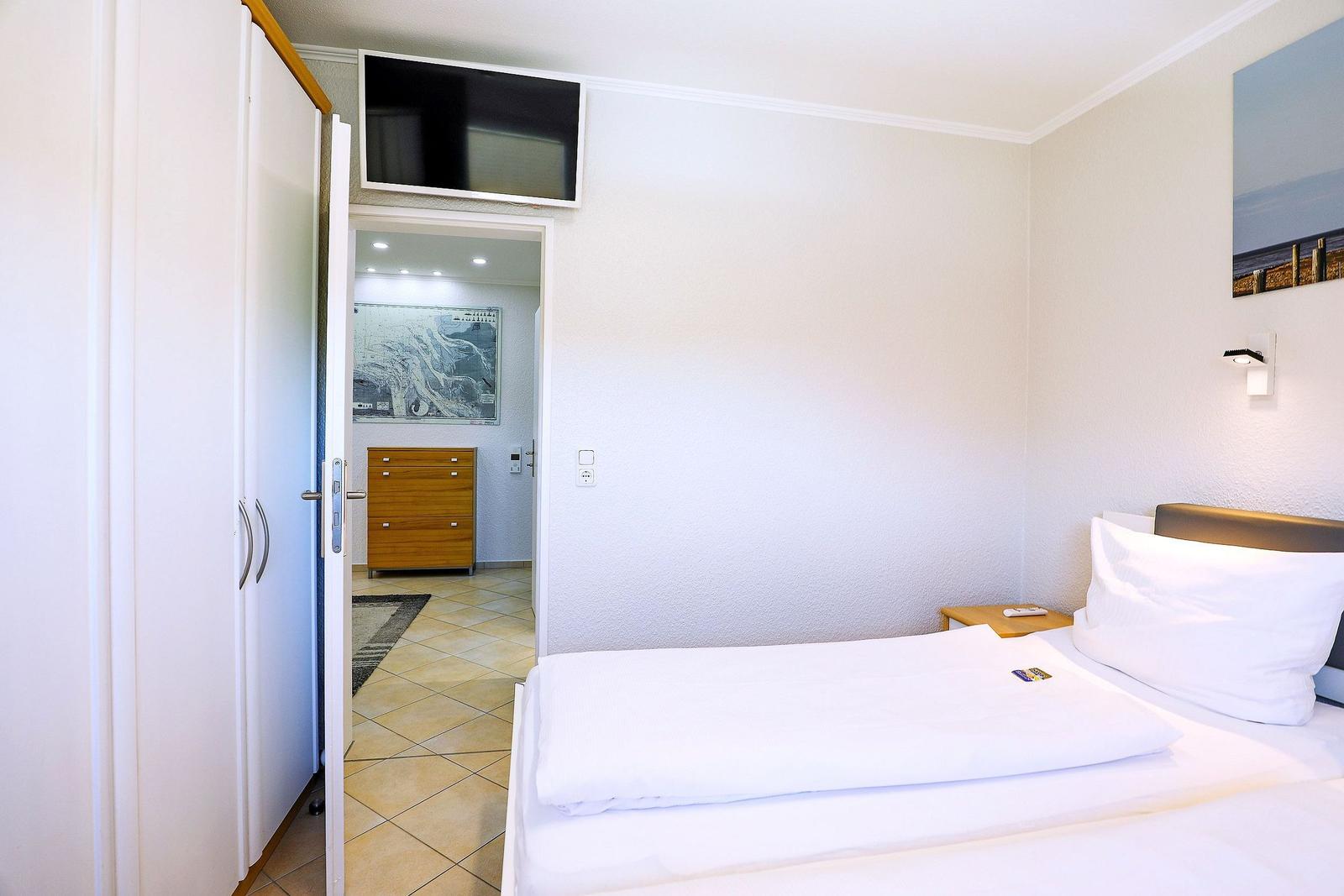 Schlafzimmer mit Bett, Fernseher und Tür zum Flur.
