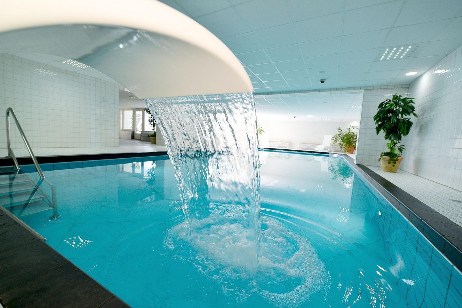 Innenpool mit Wasserfall, weiße Wände, Pflanzen und Metalltreppe