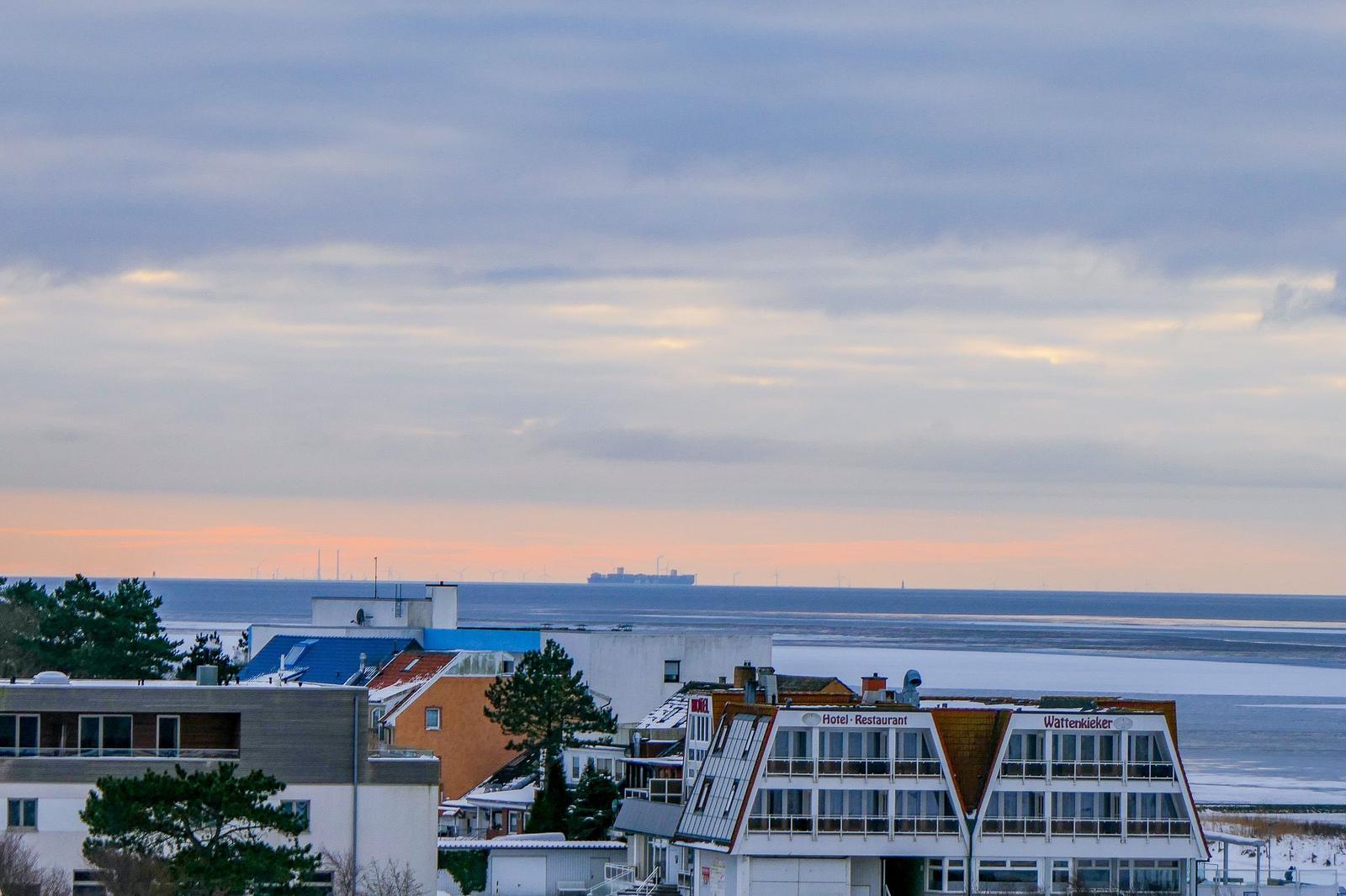 Panoramablick aufs Meer mit Hotel und Windkraftanlagen am Horizont.