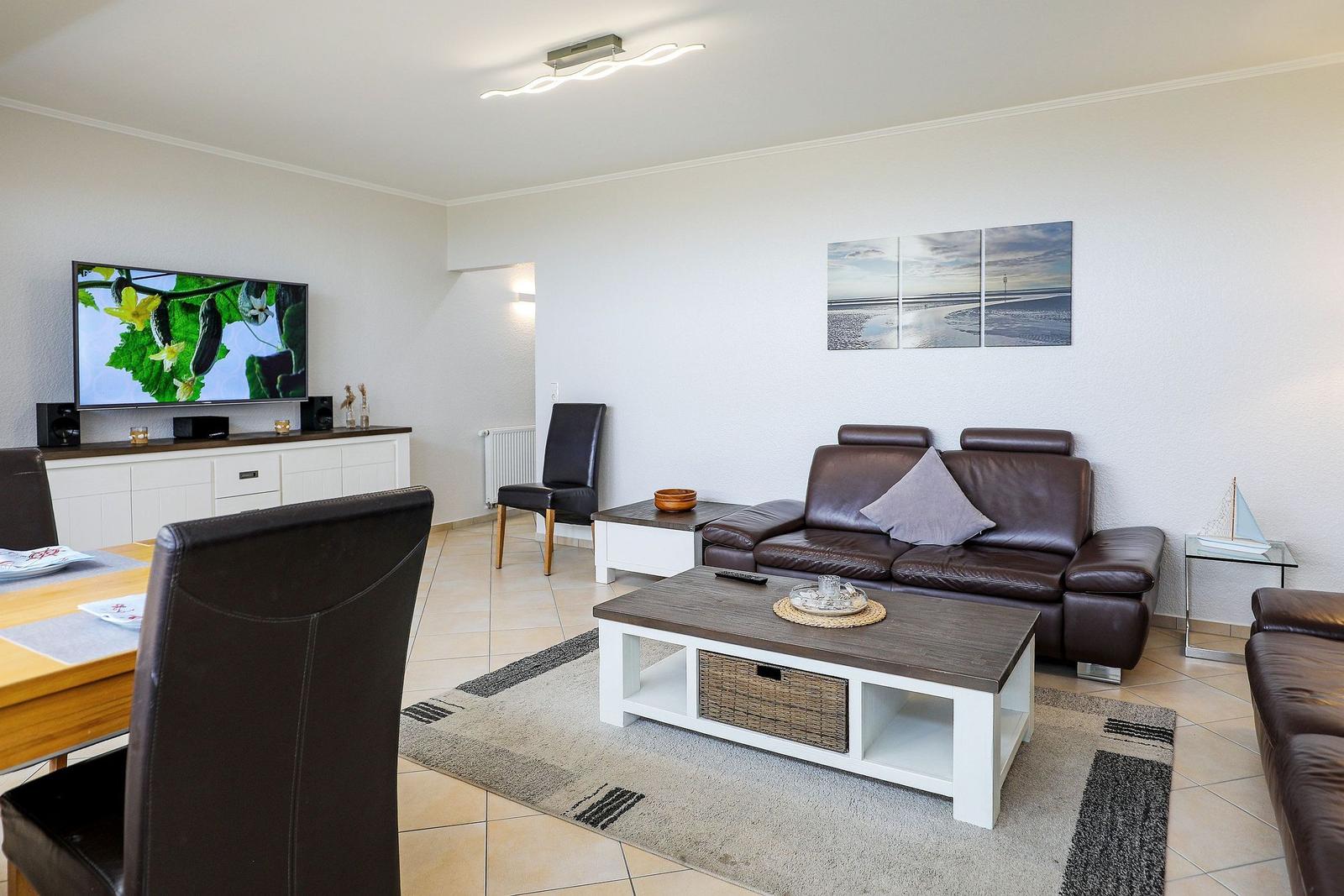 Wohnzimmer mit braunem Sofa, Fernseher und Wohnbereich.
