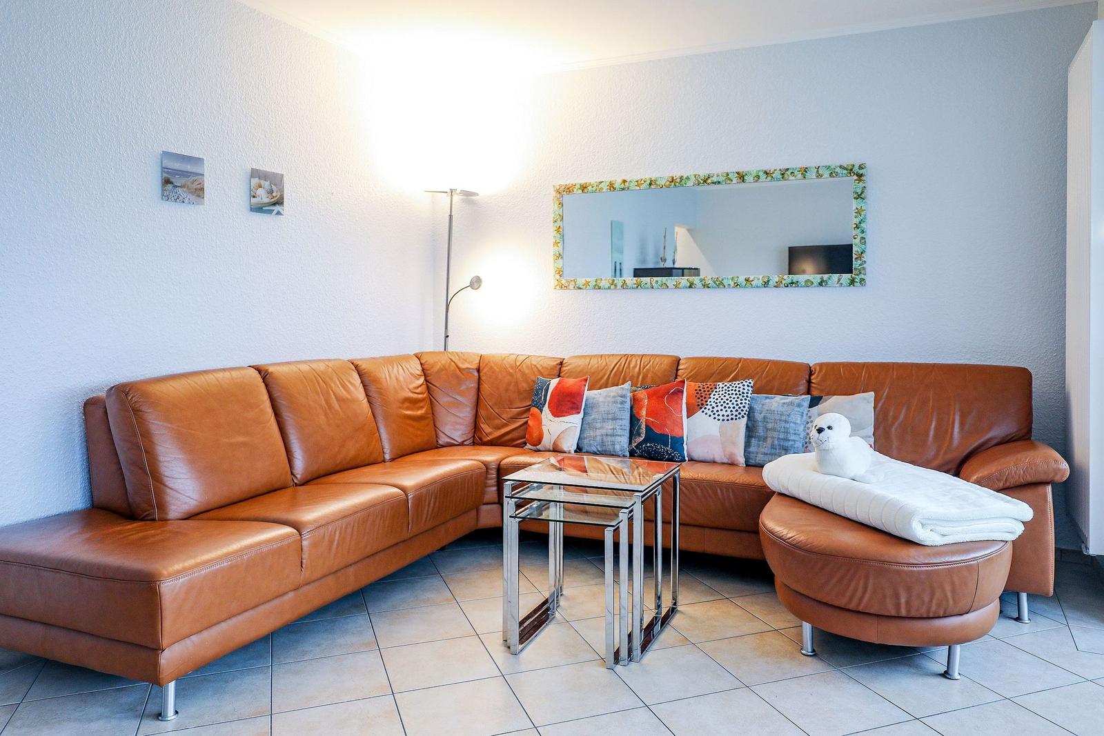 Ein Wohnzimmer mit braunem Ledersofa, Glas-Tisch und Spiegel an der Wand.