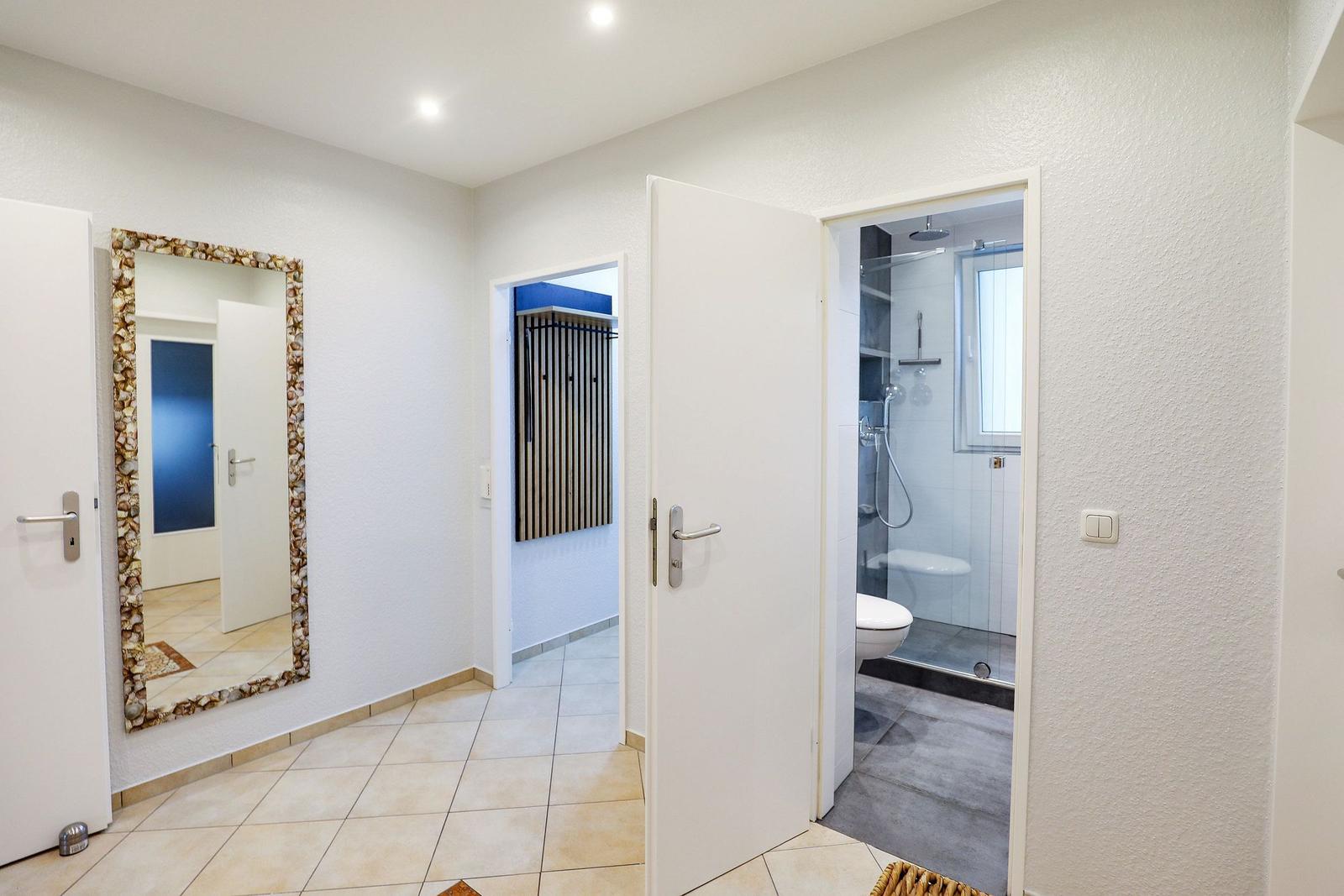 Flur mit Spiegel, Bad und Garderobe. Fliesenboden und weiße Wände.