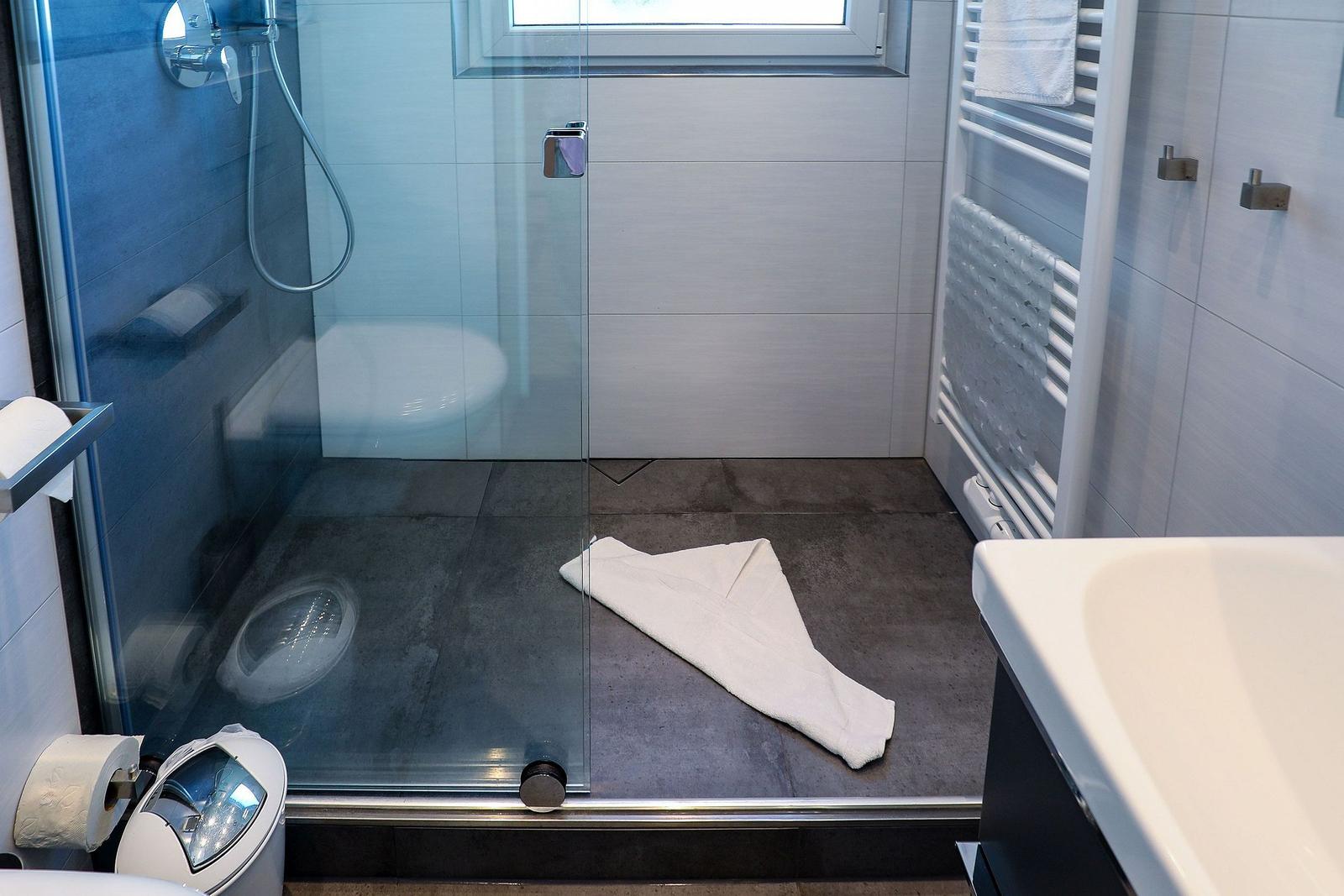 Duschkabine mit Glaswand, Toilette und Handtuch auf dem Boden.