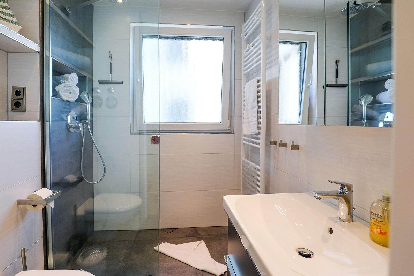 Badezimmer mit Dusche, Waschbecken und Fenster.