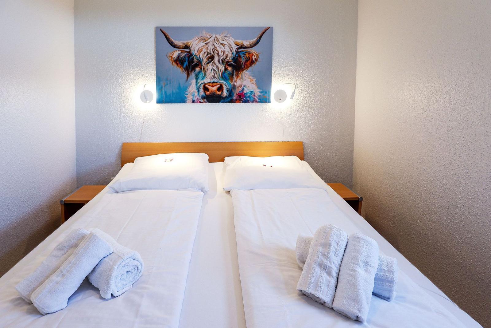 Schlafzimmer mit Doppelbett, zwei Nachttischen und Wandbild eines Hochlandrindes.