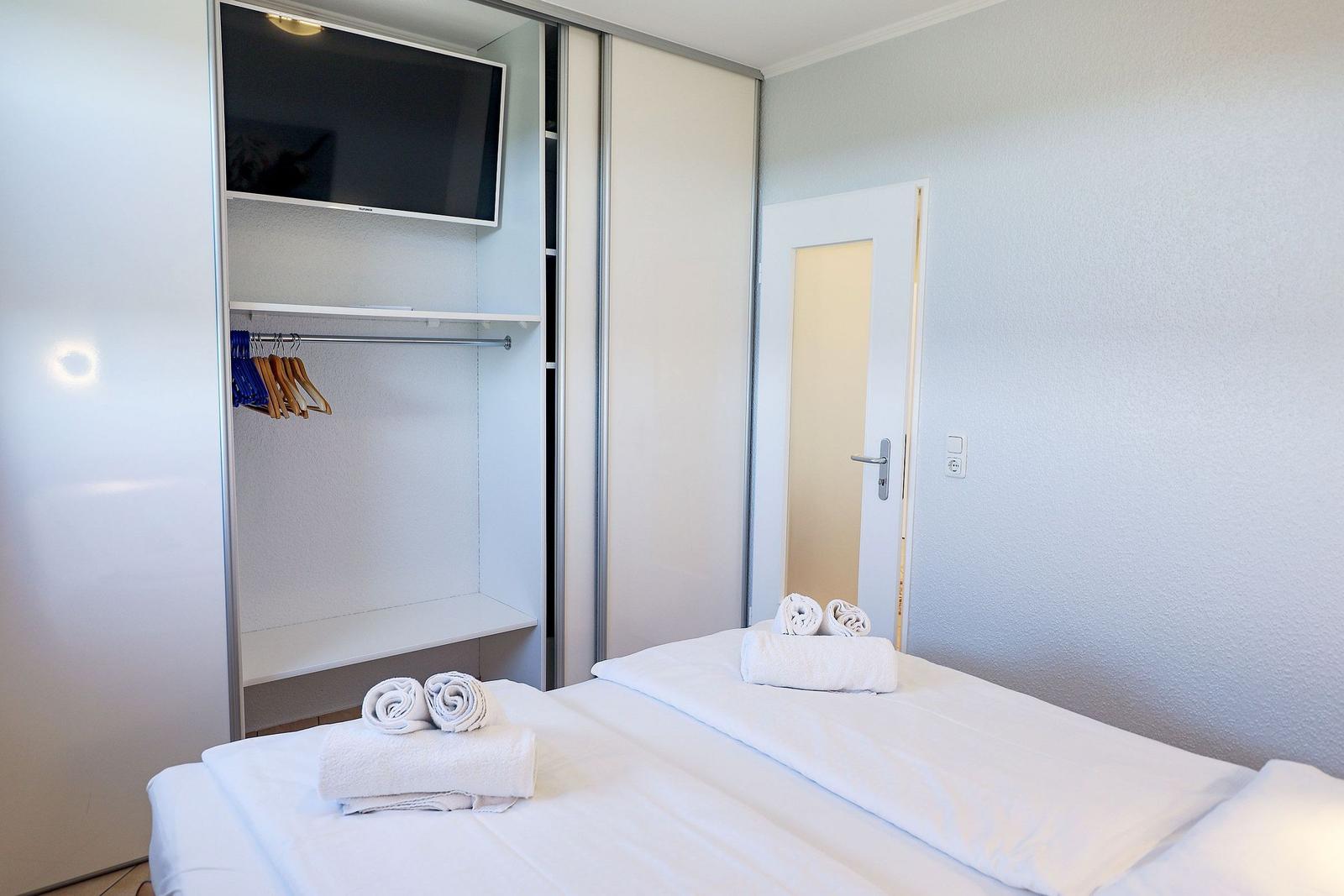 Schlafzimmer mit Bett, Kleiderschrank und Fernseher. Handtücher auf dem Bett.