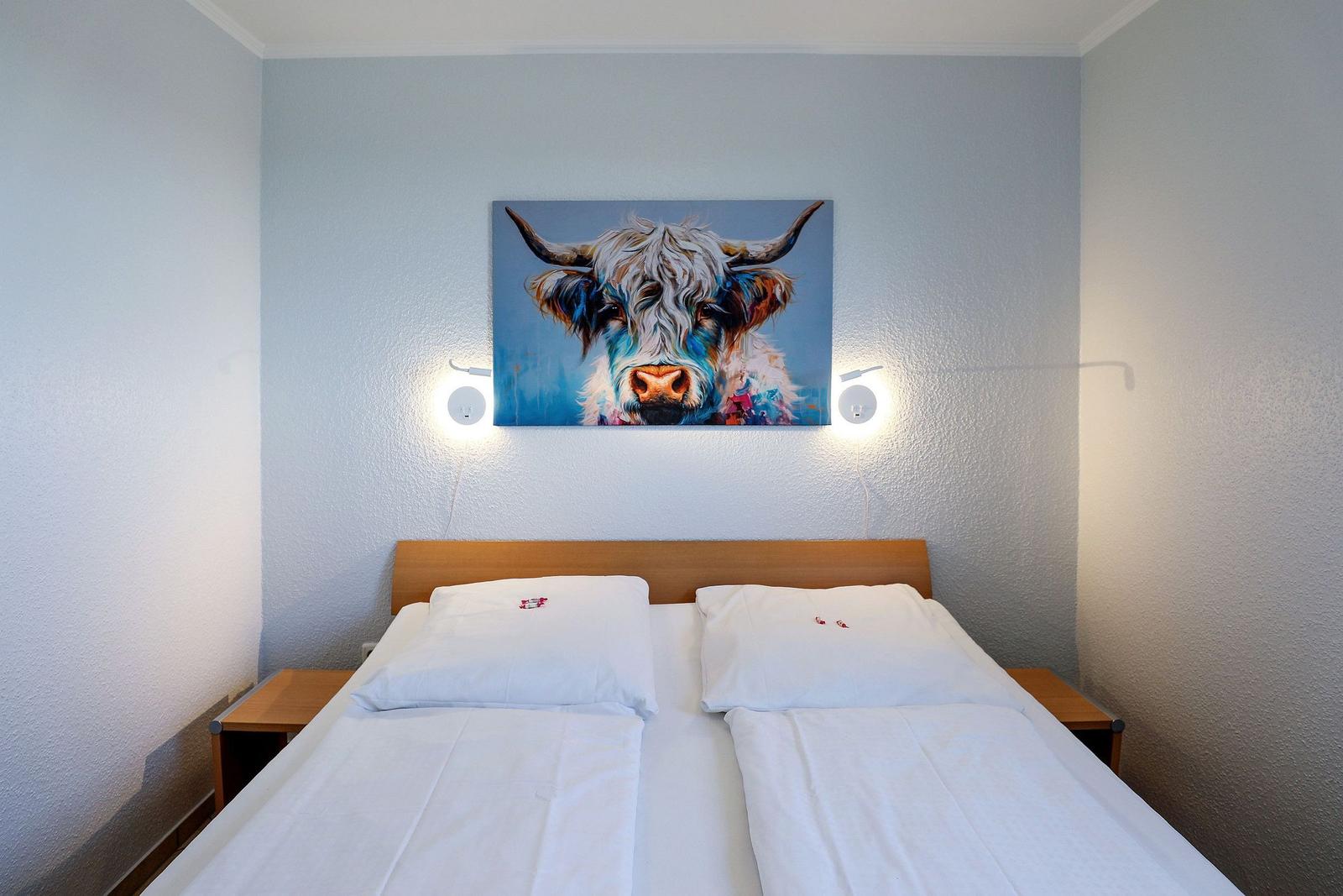 Ein Bett mit weißen Bettwäsche und einem Wandbild eines Hochlandrindes.