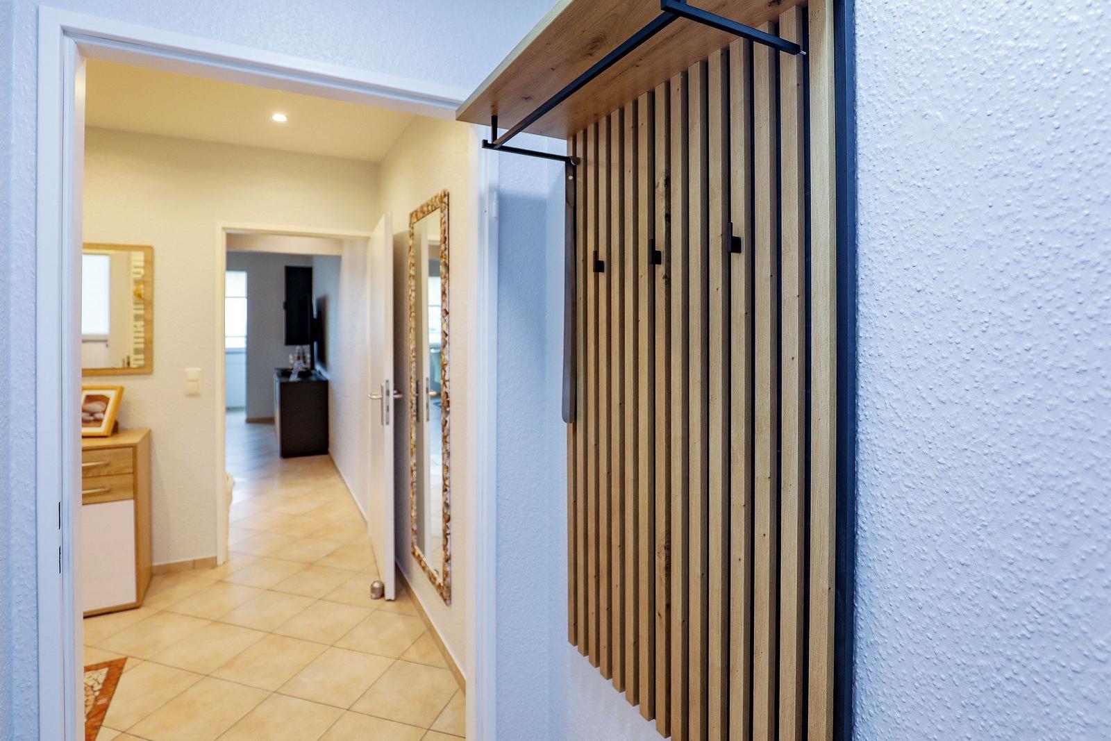 Eingangsbereich mit Holzgarderobe und Blick in den Flur mit Spiegel und Schrank.