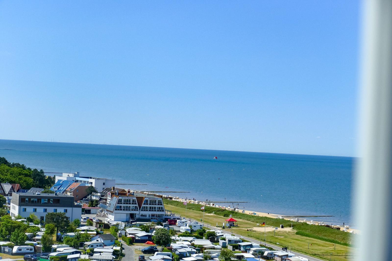 Meerblick mit Strand, Campingplatz und Windkraftanlagen im Hintergrund.