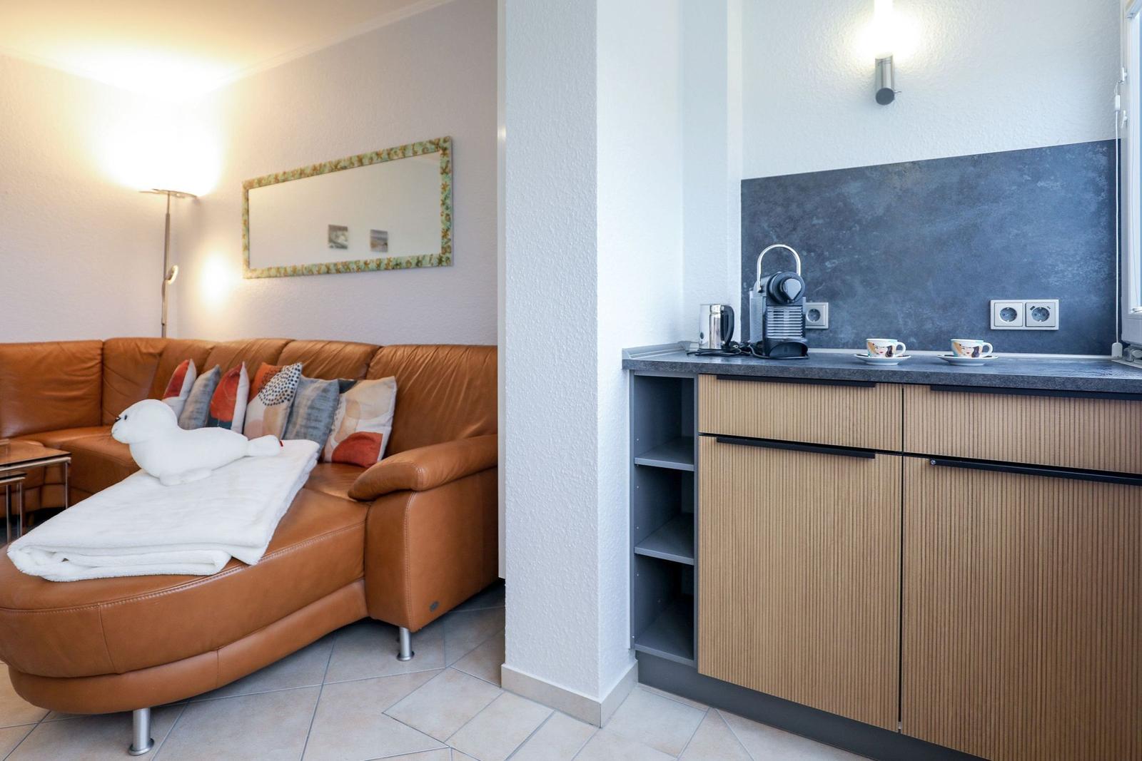 Wohnbereich mit braunem Sofa und Küchenzeile mit Kaffeemaschine.
