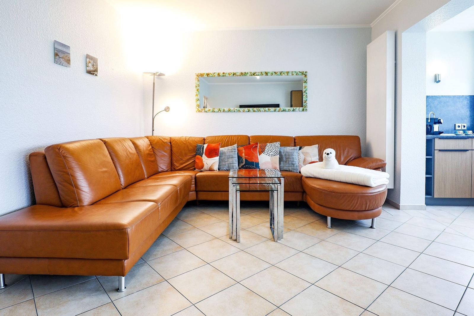 Wohnzimmer mit braunem Ledersofa, Glas-Tisch und Spiegel an der Wand.