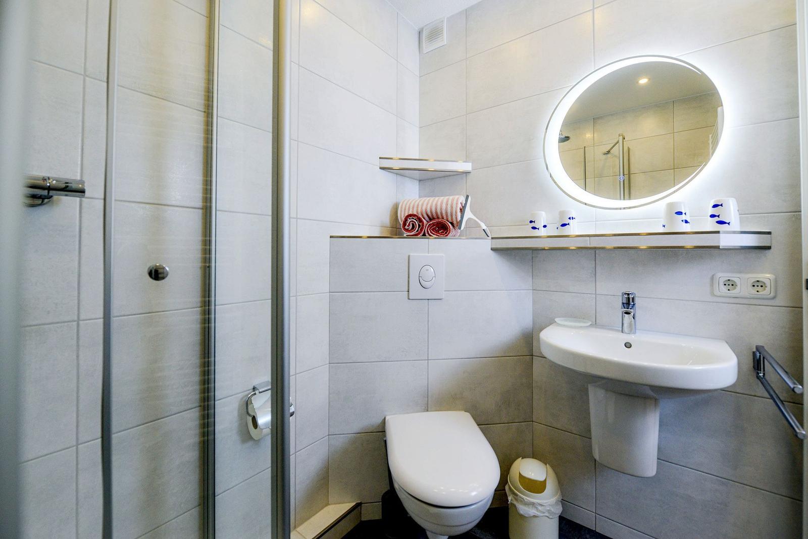 Badezimmer mit Dusche, Toilette und Waschbecken mit beleuchtetem Spiegel.