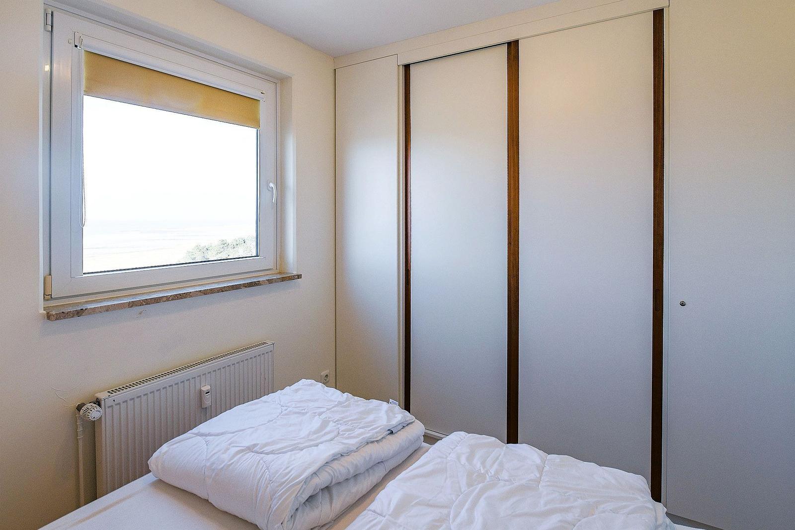 Schlafzimmer mit Bett, Kleiderschrank und Fenster mit Blick aufs Meer.