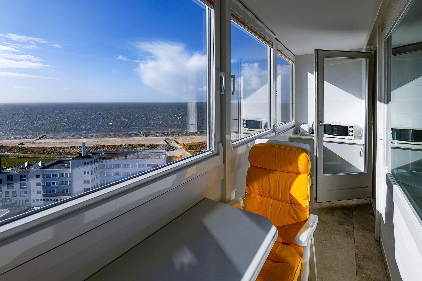 Balcony with orange chair and sea view through large windows.