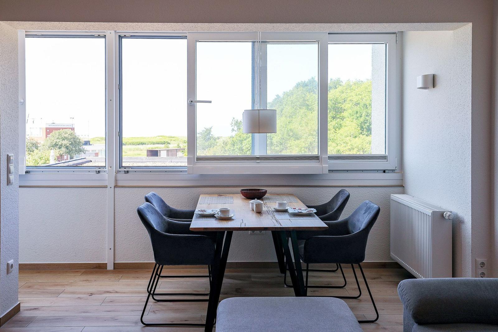 Essbereich mit Tisch und Stühlen vor großem Fenster mit Blick auf Grünflächen.