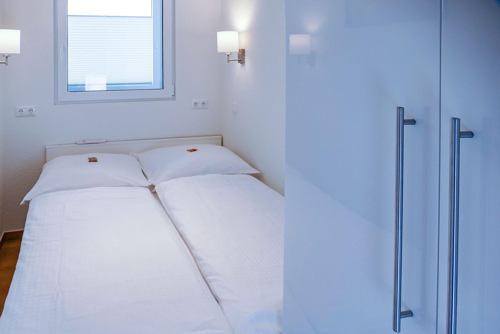 Zwei Betten mit weißen Bettwäsche, Fenster mit Jalousie und Wandlampen.