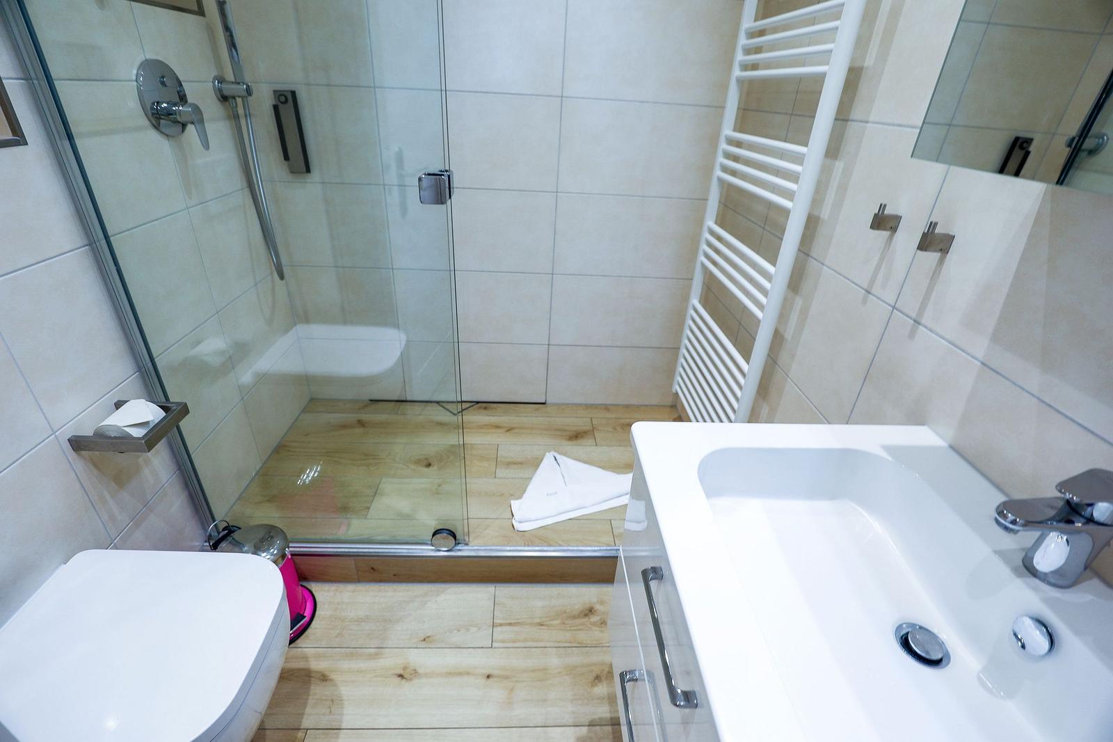Badezimmer mit Dusche, Waschbecken und Toilette auf Holzdielen.
