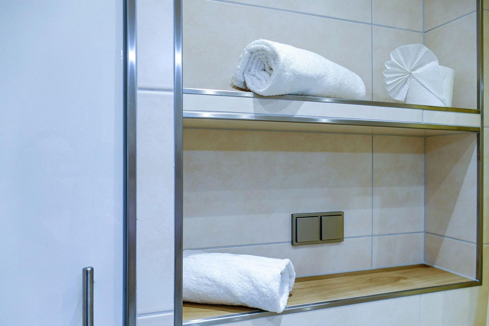 Badezimmer mit zwei weißen Handtüchern auf Holz- und Metallregalen.