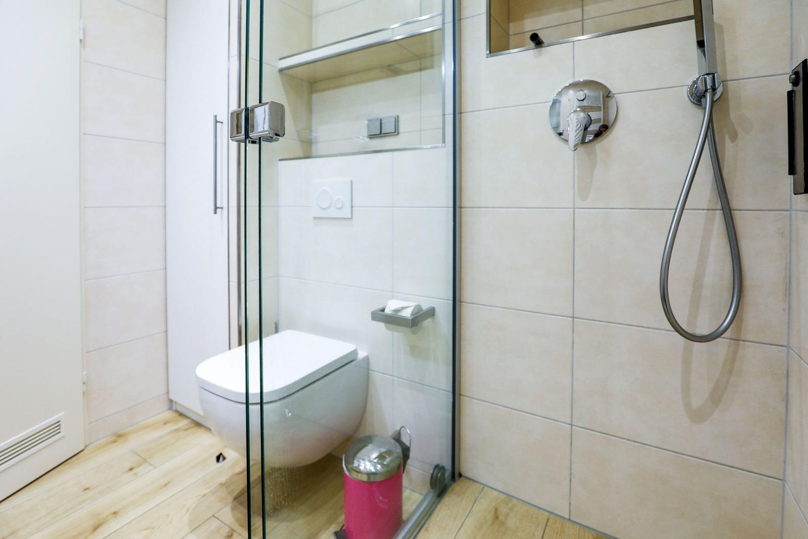 Bad mit Dusche, Toilette und pinkem Mülleimer auf Holzboden