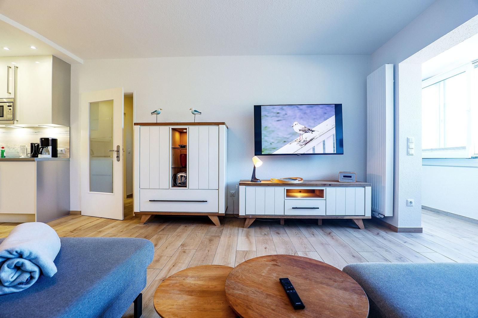 Wohnzimmer mit TV, Couch und Küchenbereich. Holzboden und moderne Möbel.