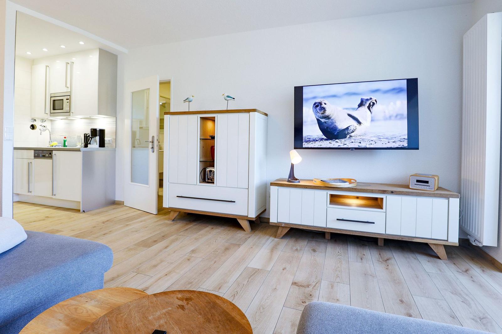 Wohnzimmer mit TV, Sideboard und Küchenbereich im Hintergrund.