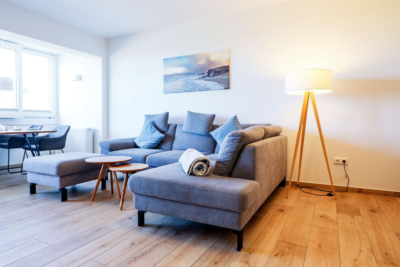 Wohnzimmer mit Sofa, Beistelltisch und Stehlampe. Holzdielenboden und Wandbild mit Strandmotiv.