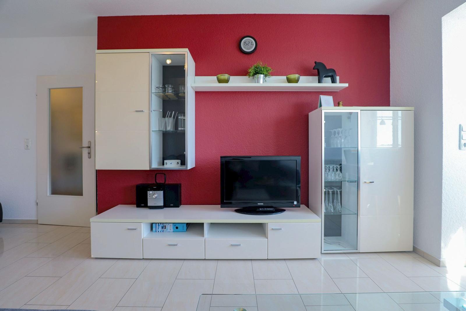 Wohnzimmer mit roter Wand, weißen Schränken und Fernseher.