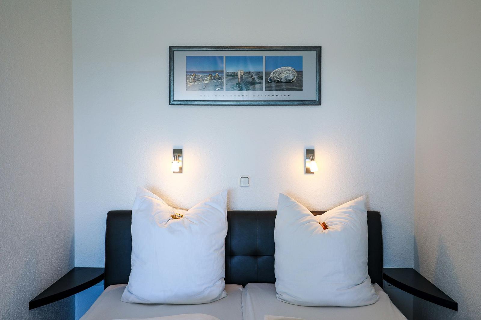 Schlafzimmer mit Bett, zwei Kissen und Wandbild über dem Kopfteil.