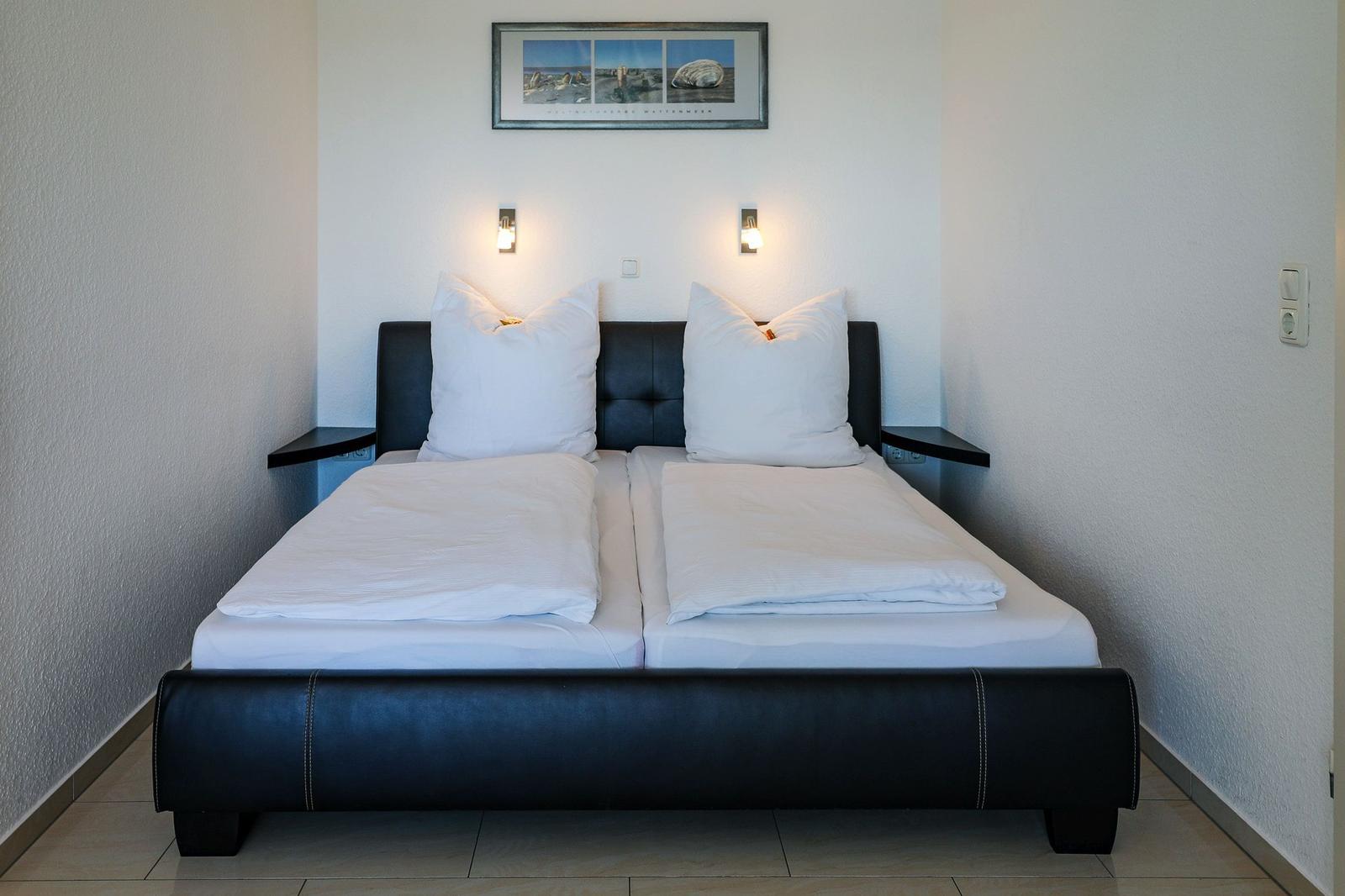 Schlafzimmer mit Doppelbett, schwarzer Kopf- und Fußteil, weißen Kissen und Decken.