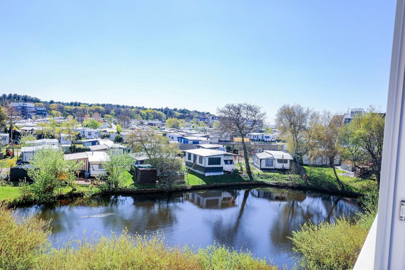 Panorama mit Kanal, Grünflächen und Wohnwagen im Hintergrund unter blauem Himmel.