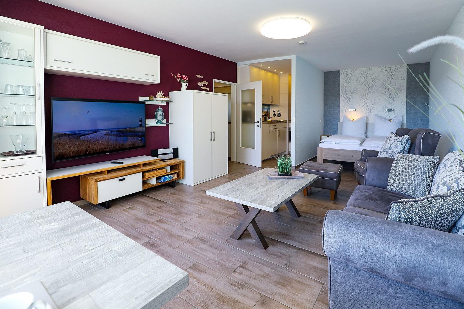 Wohnbereich mit Sofa, TV und Küchenbereich im Hintergrund.