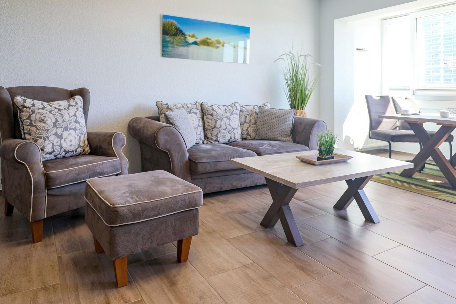 Wohnzimmer mit Sofa, Sessel und Couchtisch. Holzboden und Wandbild sichtbar.