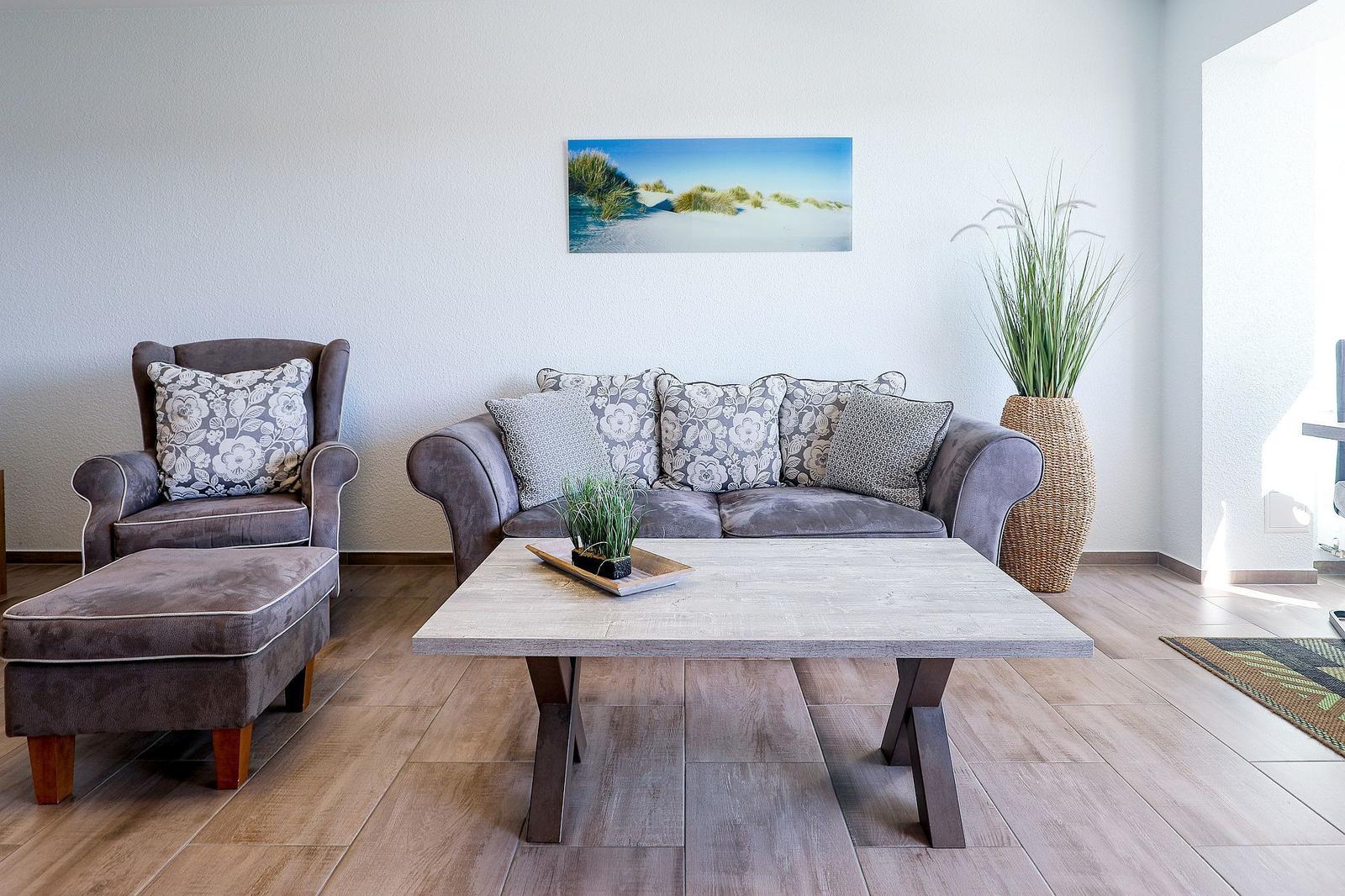 Wohnzimmer mit Sofa, Sessel und Tisch. Wandbild und Pflanze sichtbar.