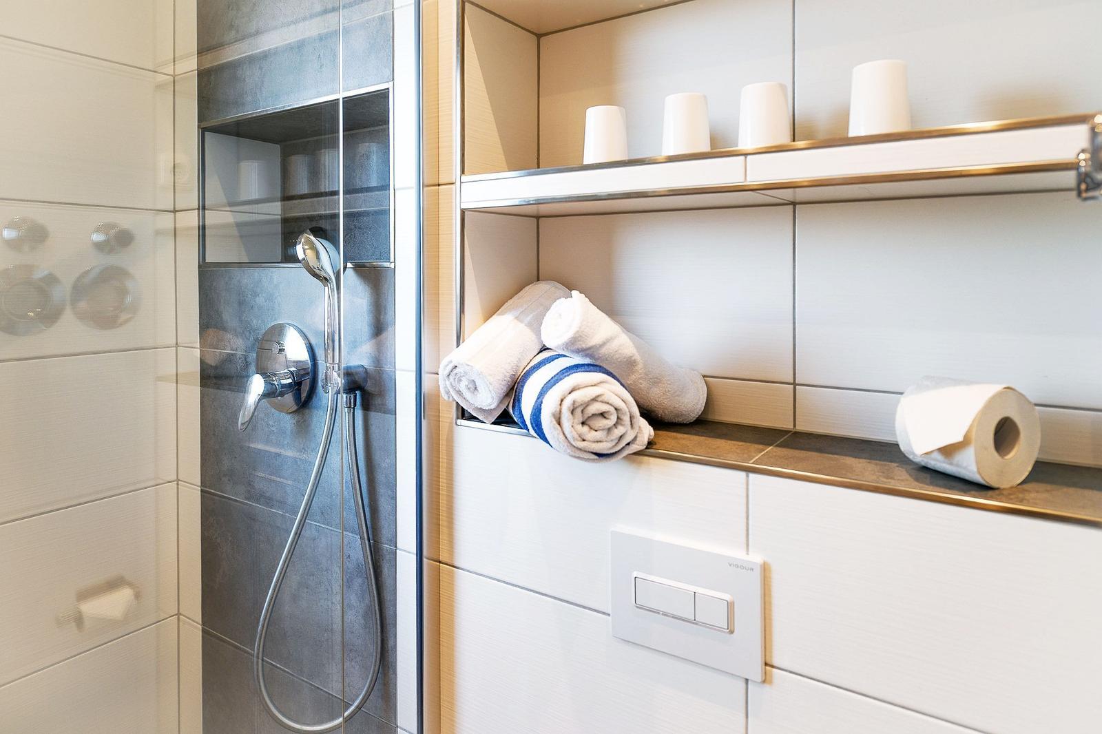 Dusche mit Duschbrause und Handtuchregal mit Handtüchern.