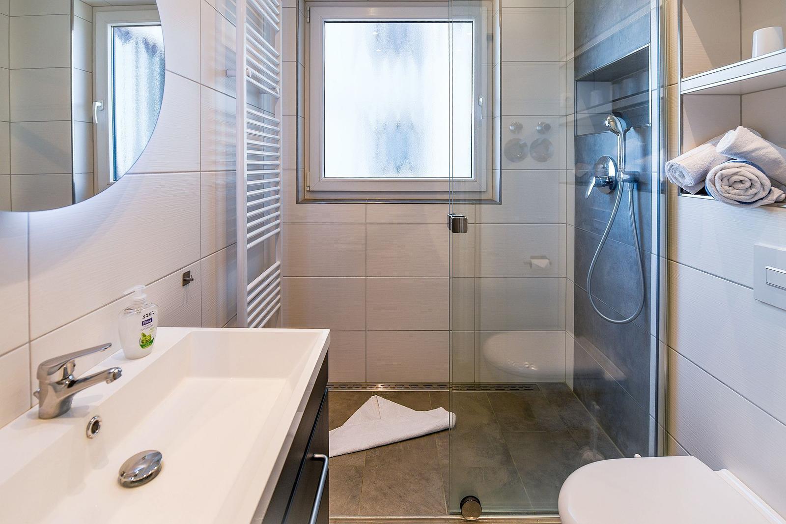 Badezimmer mit Dusche, Waschbecken und Toilette. Fenster mit Milchglas.