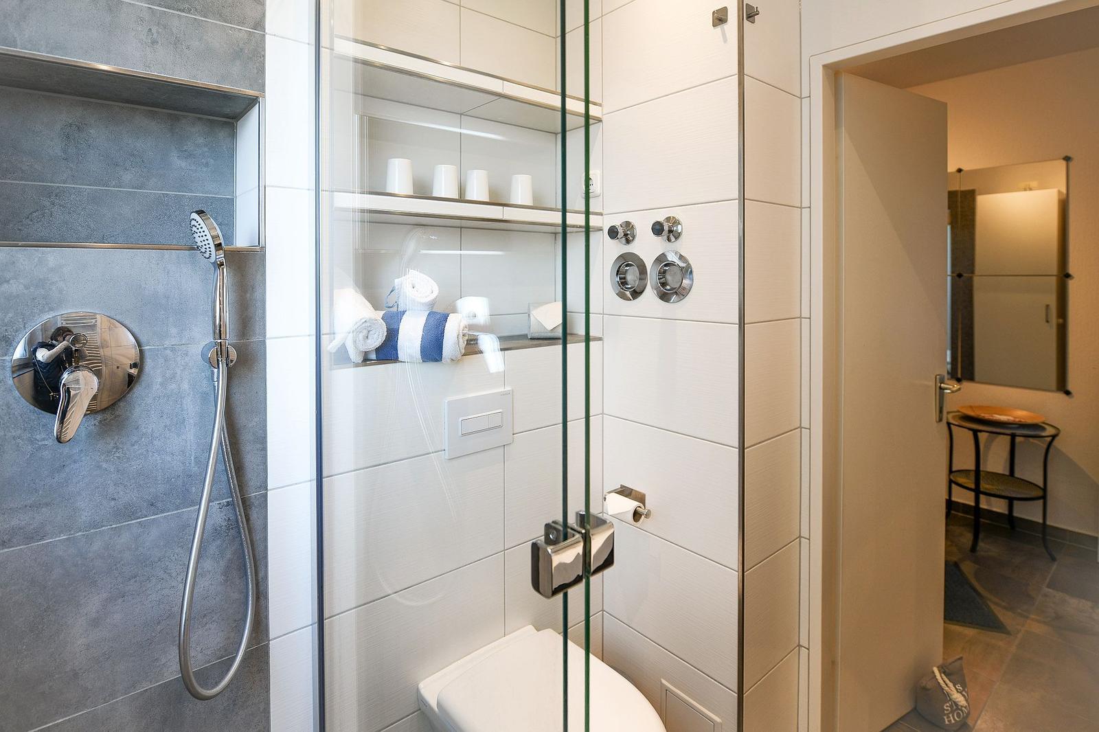 Dusche mit Glaswand, Toilette und Regal mit Handtüchern und Tassen